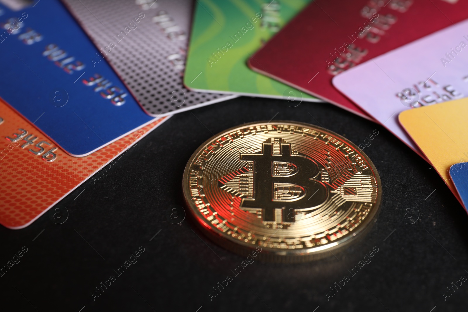 Photo of Bitcoin and plastic bank cards on black background, closeup