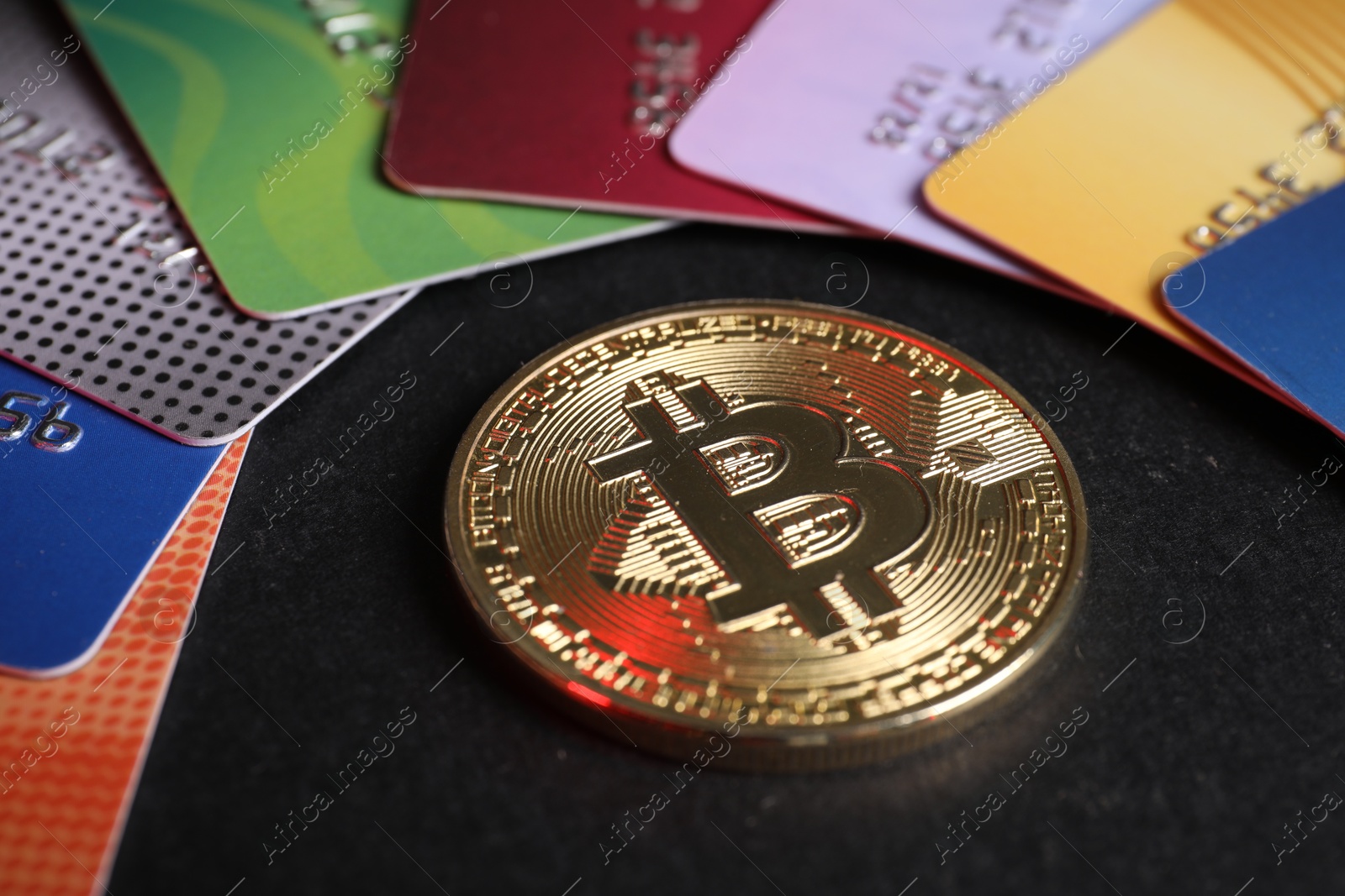 Photo of Bitcoin and plastic bank cards on black background, closeup