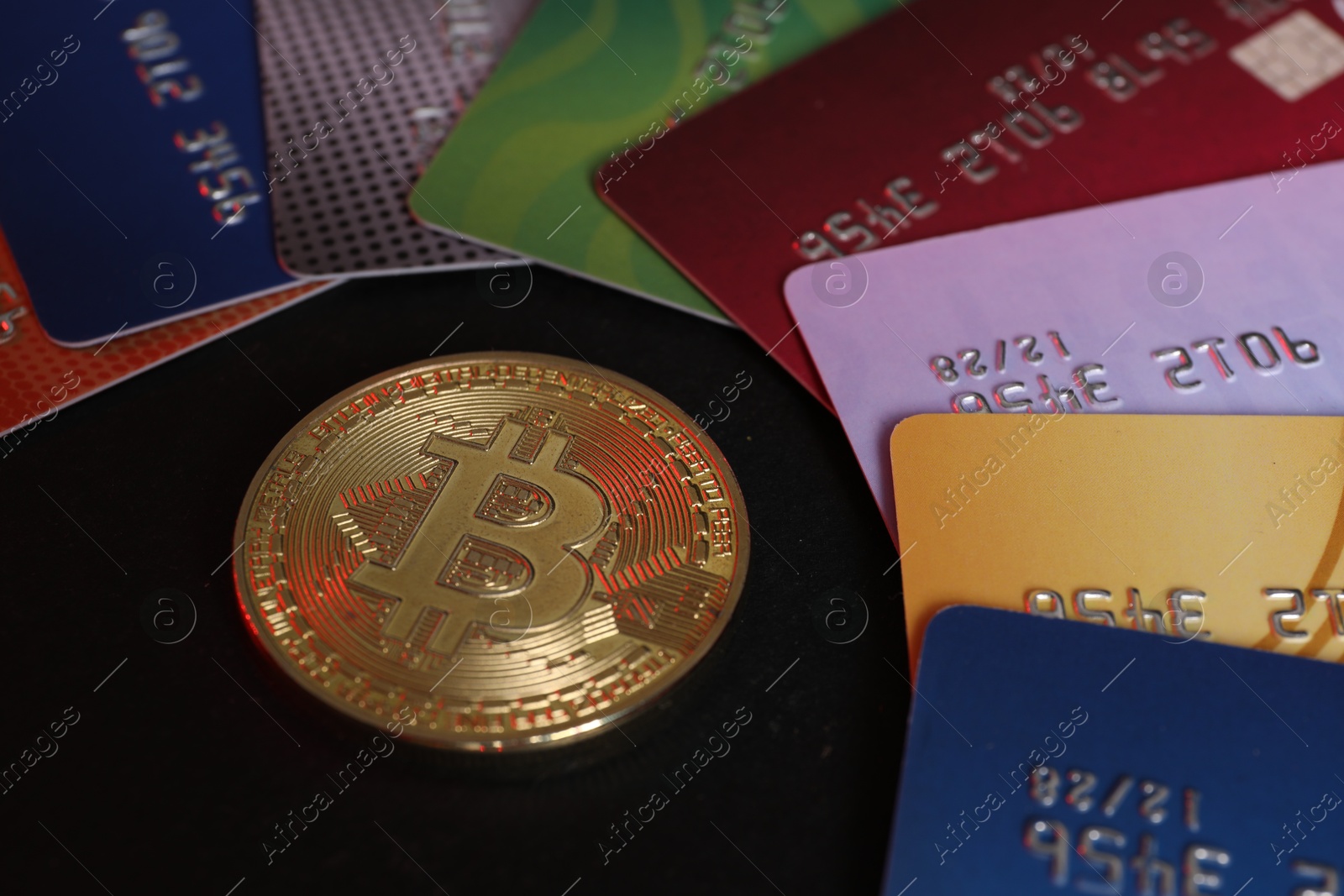 Photo of Bitcoin and plastic bank cards on black background, closeup