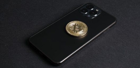 Photo of Smartphone with bitcoin on black background, closeup