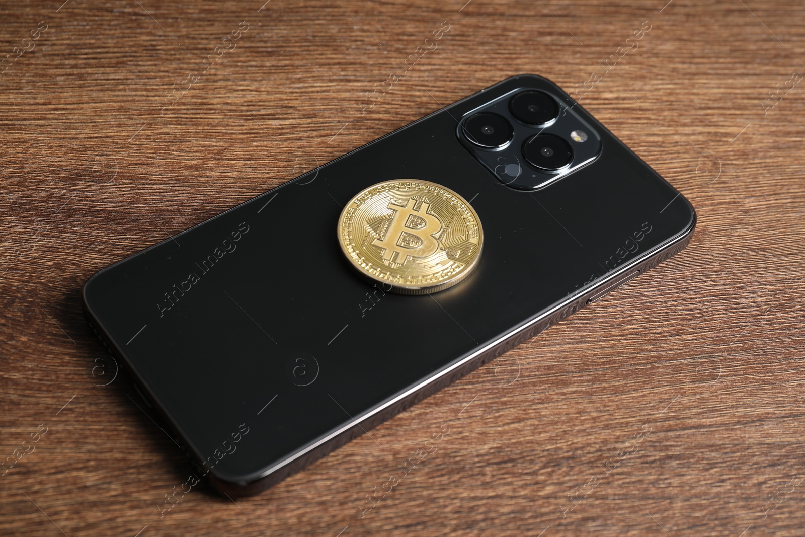 Photo of Smartphone with bitcoin on wooden table, closeup