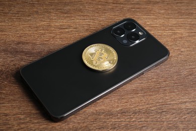 Photo of Smartphone with bitcoin on wooden table, closeup