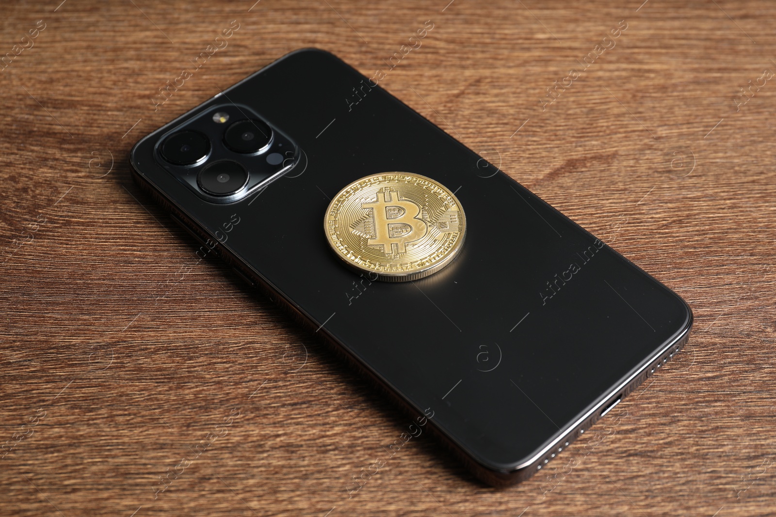 Photo of Smartphone with bitcoin on wooden table, closeup
