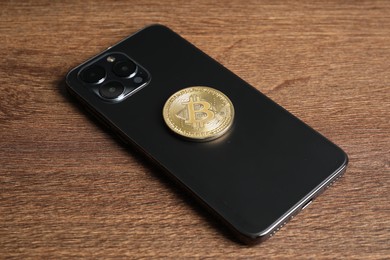 Photo of Smartphone with bitcoin on wooden table, closeup