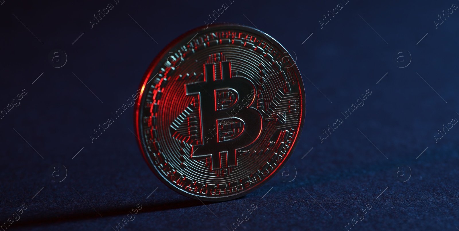 Photo of Bitcoin on blue background in red light, closeup