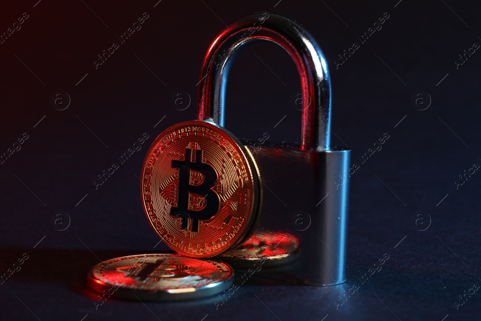 Photo of Bitcoins and padlock on blue background in red light, closeup