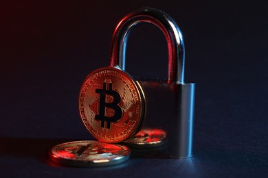 Photo of Bitcoins and padlock on blue background in red light, closeup