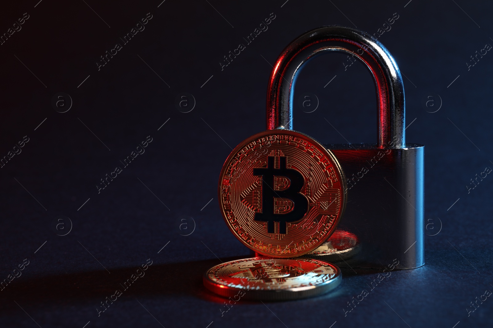 Photo of Bitcoins and padlock on blue background in red light, closeup with space for text
