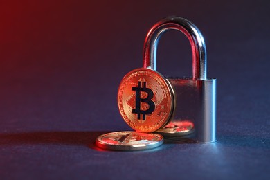 Photo of Bitcoins and padlock on blue background in red light, closeup with space for text