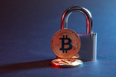 Photo of Bitcoins and padlock on blue background in red light, closeup with space for text