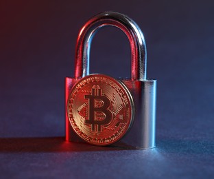 Photo of Bitcoin and padlock on blue background in red light, closeup