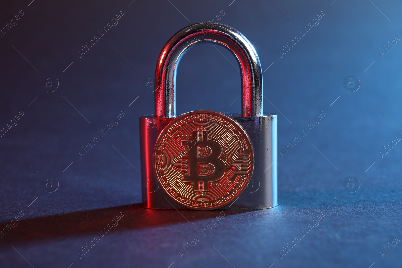 Photo of Bitcoin and padlock on blue background in red light, closeup