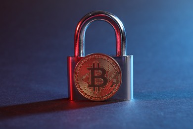Photo of Bitcoin and padlock on blue background in red light, closeup