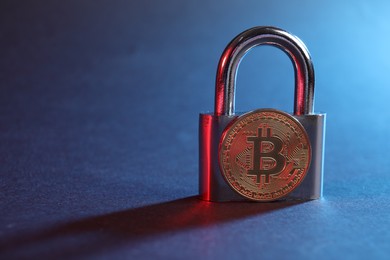 Photo of Bitcoin and padlock on blue background in red light, closeup with space for text