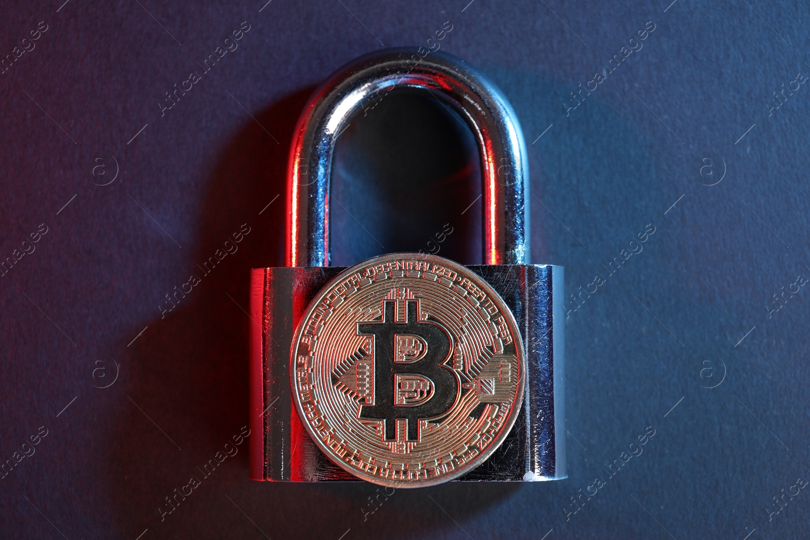 Photo of Bitcoin and padlock on blue background in red light, top view