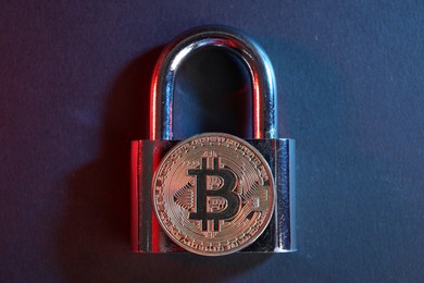 Photo of Bitcoin and padlock on blue background in red light, top view