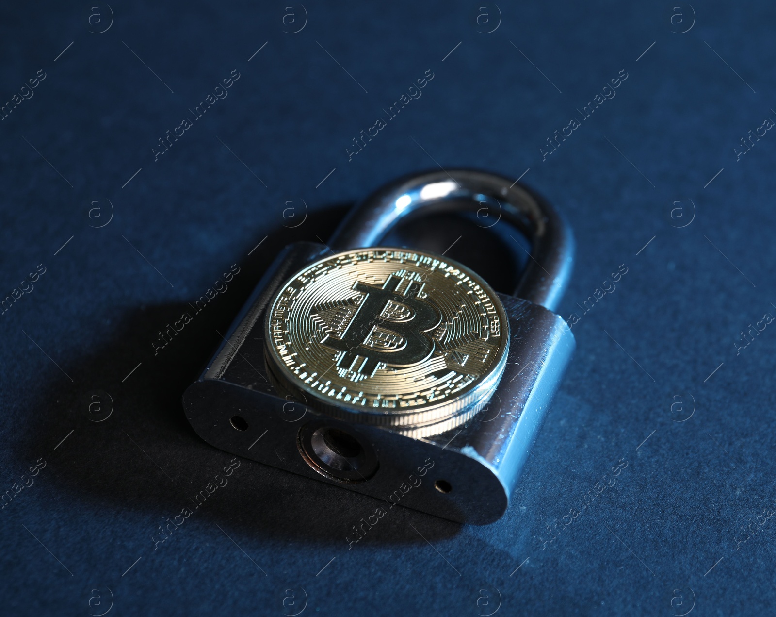Photo of Bitcoin and padlock on blue background, closeup