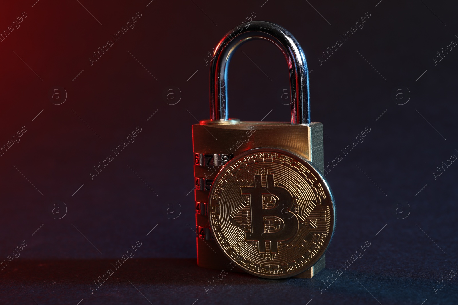 Photo of Bitcoin and padlock on blue background in red light, closeup