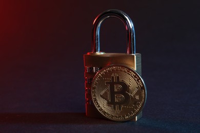 Photo of Bitcoin and padlock on blue background in red light, closeup