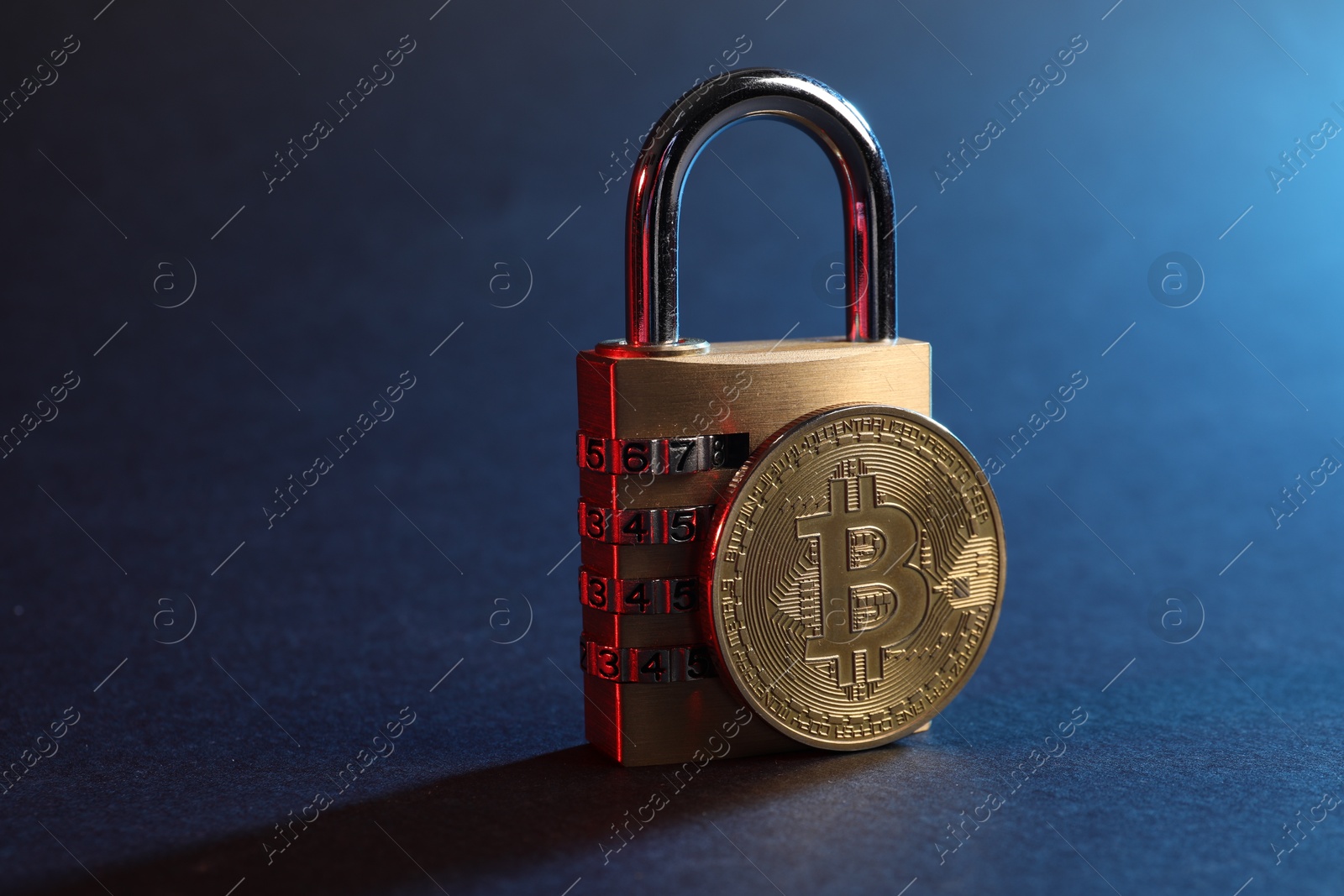 Photo of Bitcoin and padlock on blue background in red light, closeup