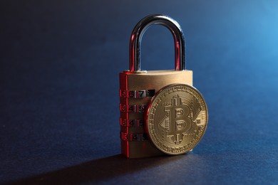Photo of Bitcoin and padlock on blue background in red light, closeup