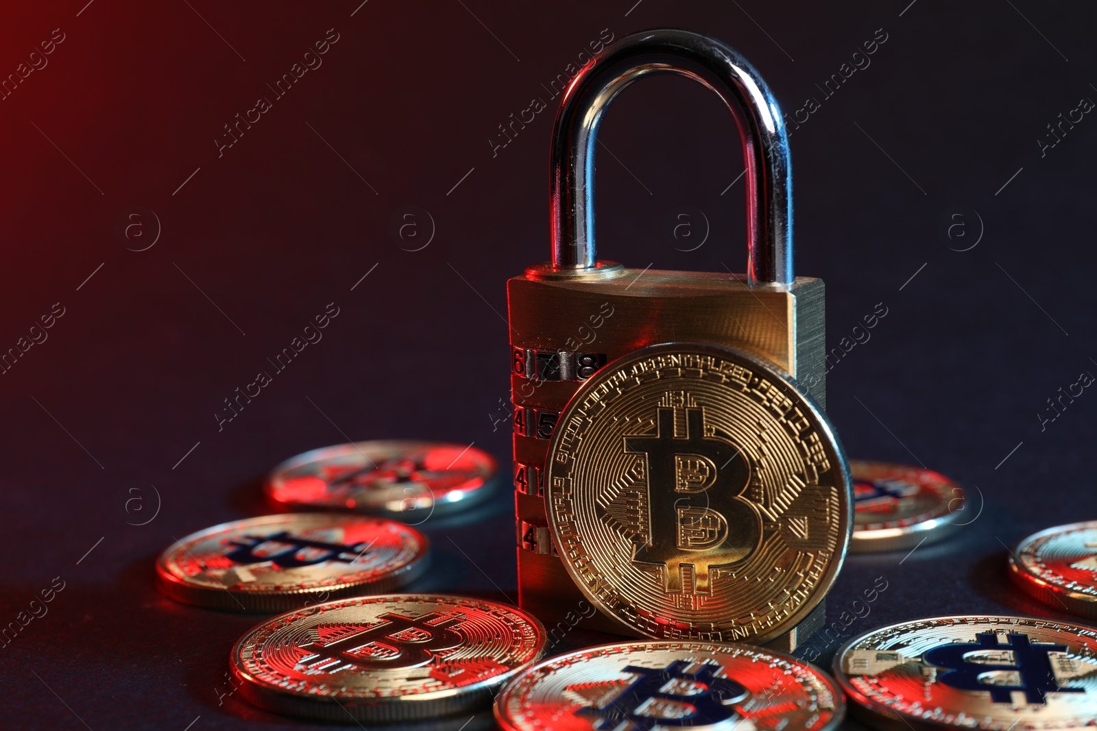 Photo of Bitcoins and padlock on blue background in red light, closeup