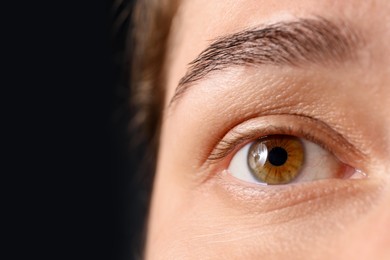 Photo of Woman with beautiful eyes on black background, closeup. Space for text