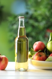 Photo of Delicious cider in glass bottle and apples on white wooden table outdoors