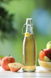 Photo of Delicious cider in glass bottle and apples on white wooden table outdoors