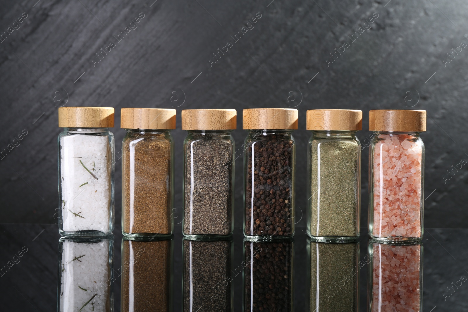 Photo of Different spices in glass jars on mirror surface