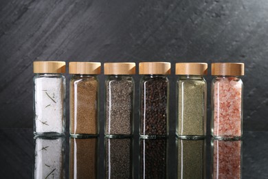 Photo of Different spices in glass jars on mirror surface
