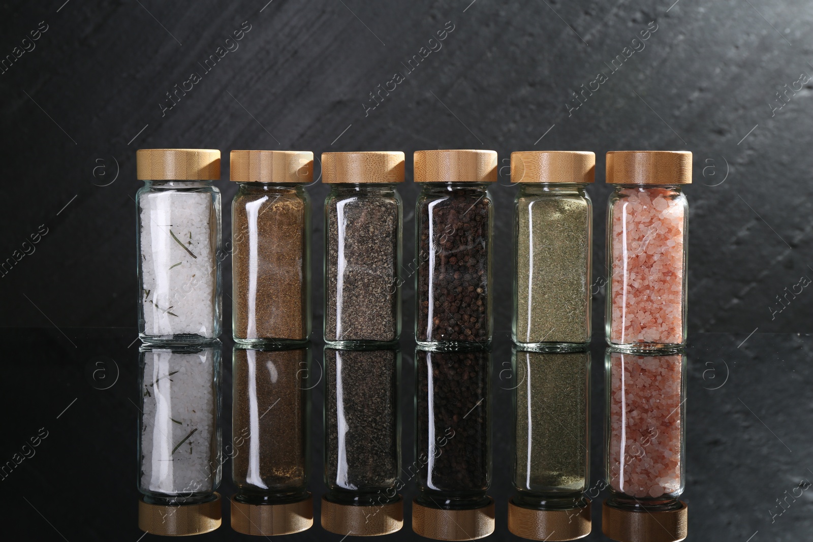 Photo of Different spices in glass jars on mirror surface