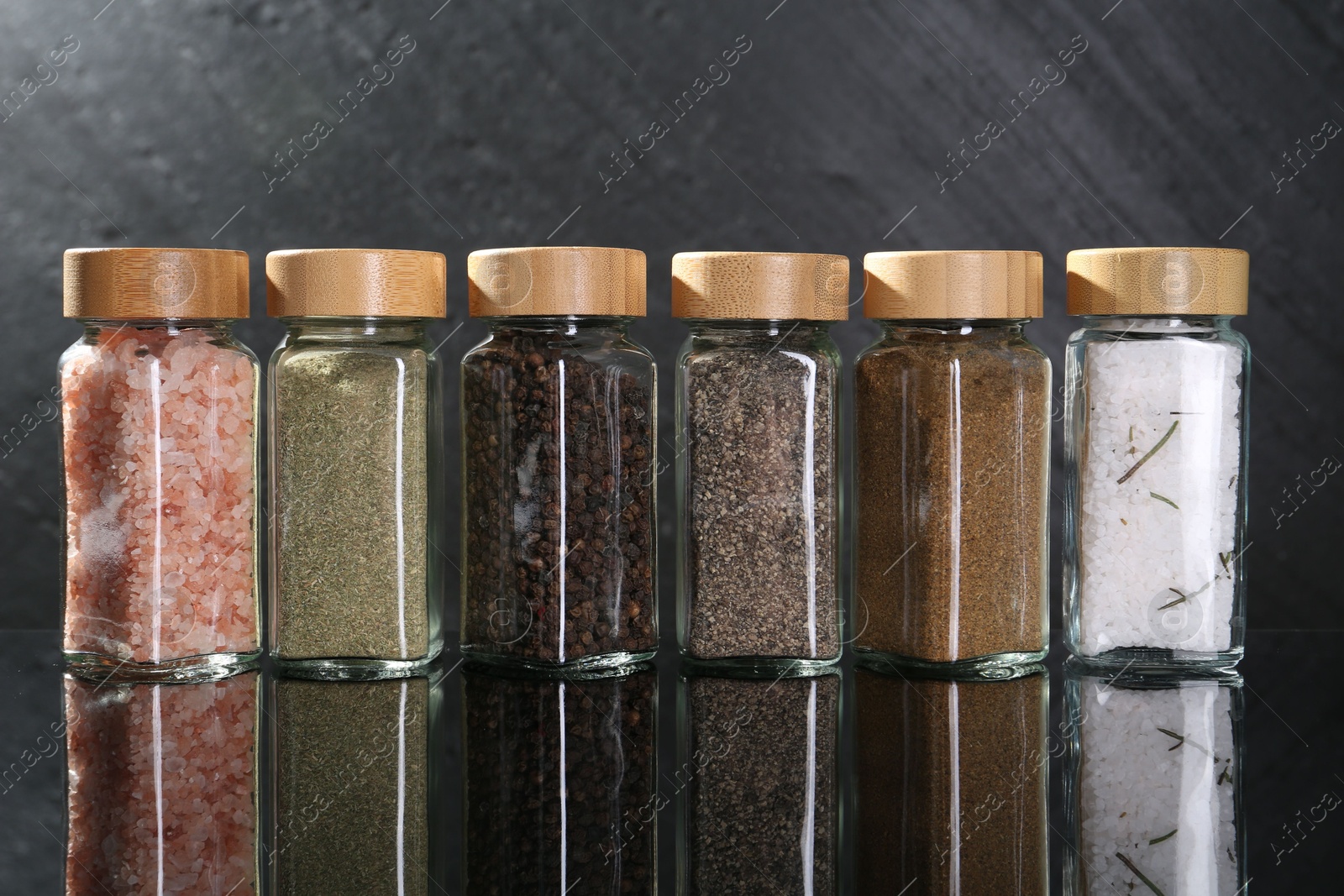 Photo of Different spices in glass jars on mirror surface