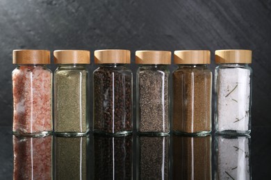 Photo of Different spices in glass jars on mirror surface