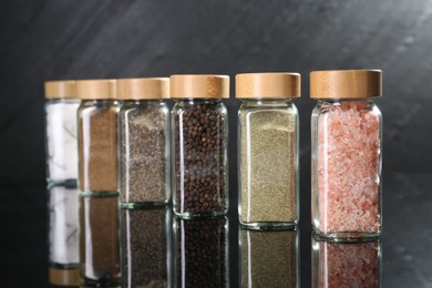 Photo of Different spices in glass jars on mirror surface, closeup