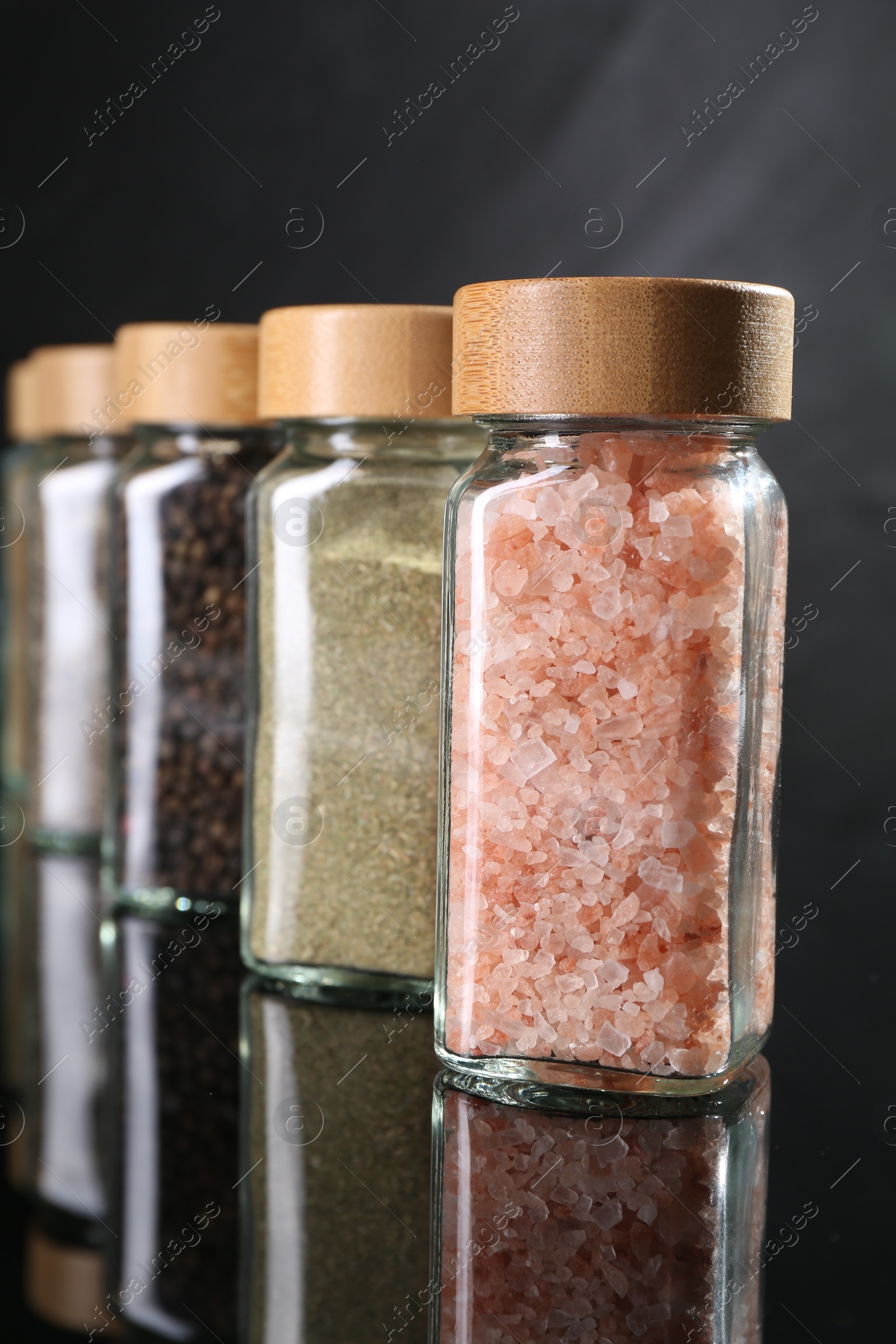 Photo of Different spices in glass jars on mirror surface, closeup