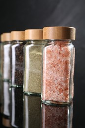 Photo of Different spices in glass jars on mirror surface, closeup
