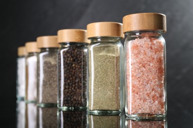 Photo of Different spices in glass jars on mirror surface, closeup