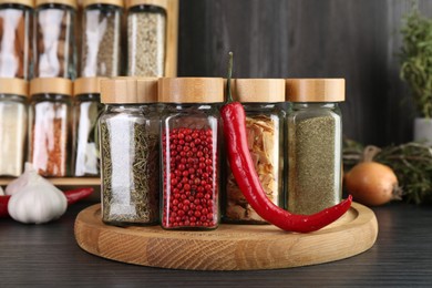 Photo of Different spices in glass jars and chili pepper on grey wooden table, closeup