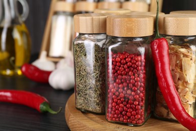 Photo of Different spices in glass jars and chili pepper on grey wooden table, closeup