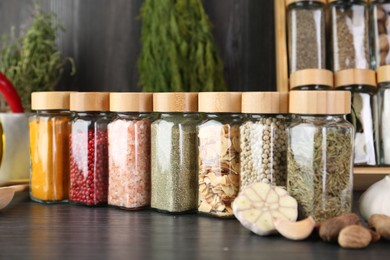 Photo of Different spices and glass jars on grey wooden table, closeup