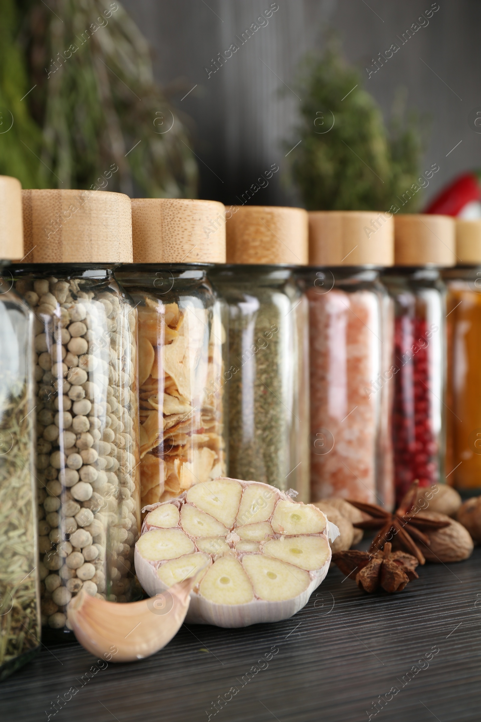 Photo of Different spices and glass jars on grey wooden table, closeup