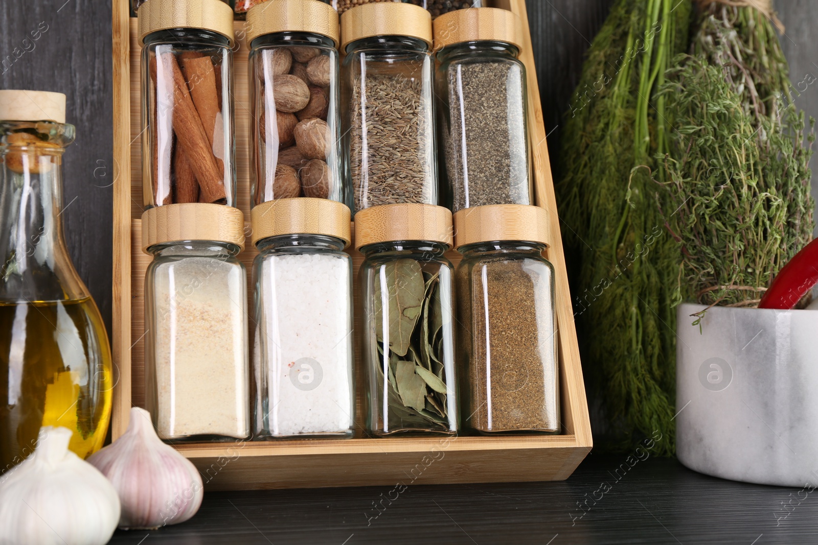 Photo of Set of different spices in glass jars on grey wooden table, closeup
