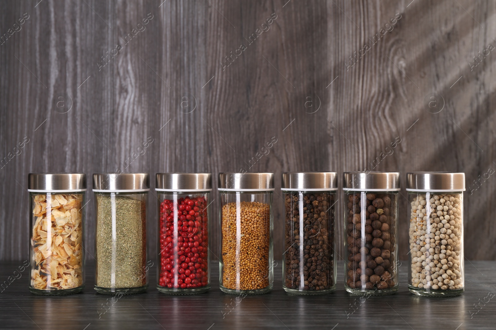 Different spices in glass jars on grey wooden table Photo of Different spices in glass jars on grey wooden table