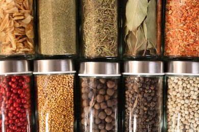 Photo of Different spices in glass jars as background, top view