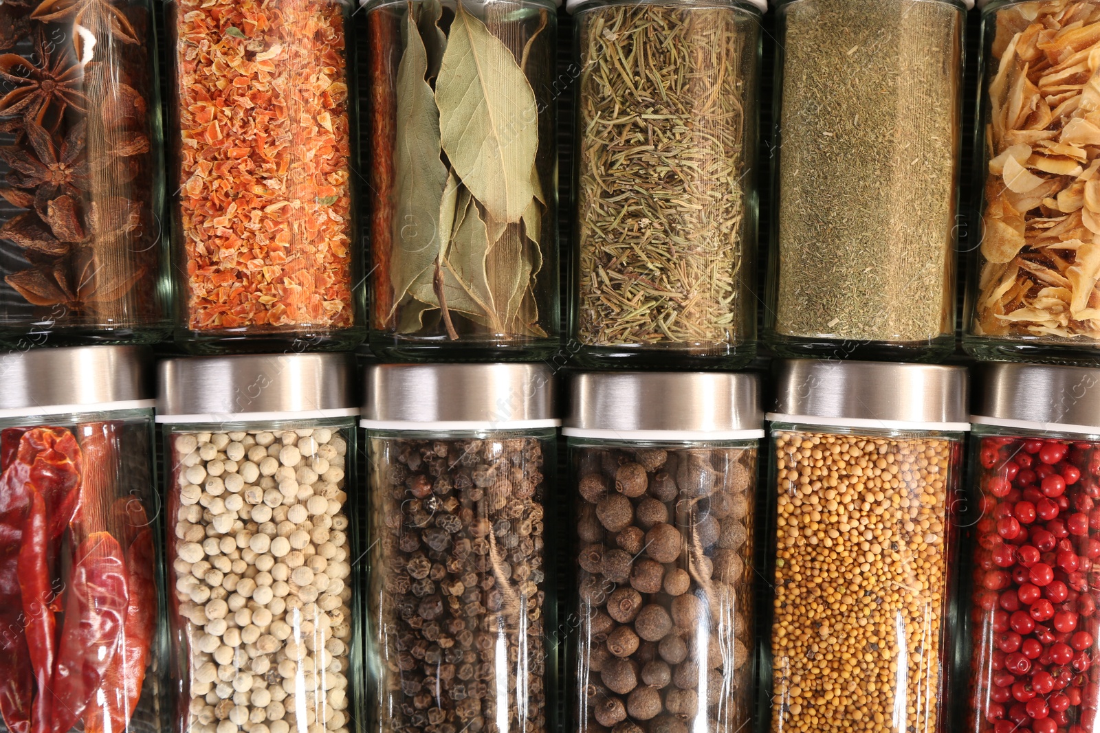 Photo of Different spices in glass jars as background, top view