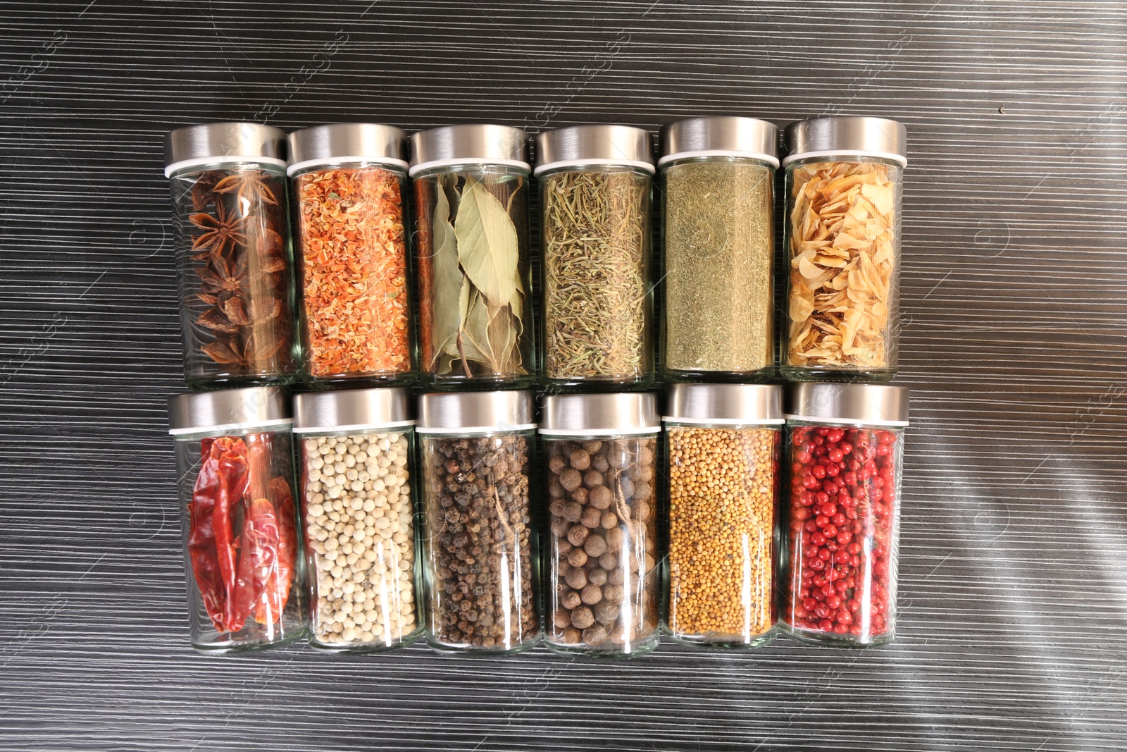 Different spices in glass jars on grey wooden table Photo of Different spices in glass jars on grey wooden table