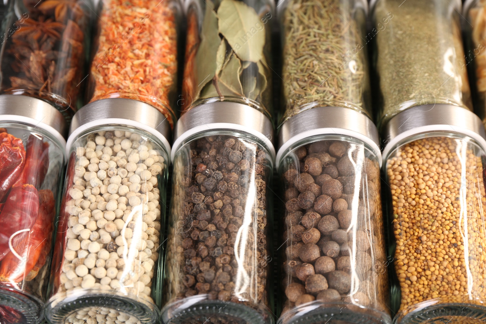 Photo of Different spices in glass jars as background, closeup