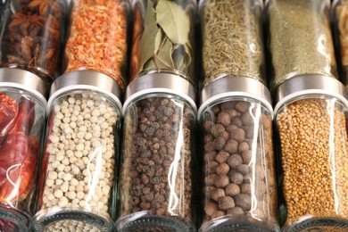 Photo of Different spices in glass jars as background, closeup