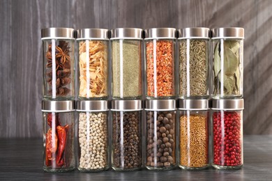 Photo of Different spices in glass jars on grey wooden table